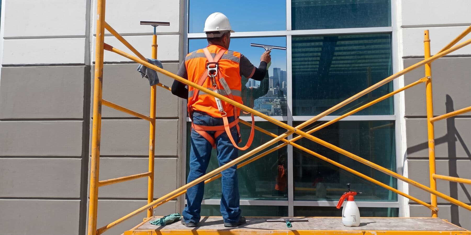 Instalador con casco y arnés terminando un muro cortina desde un andamio